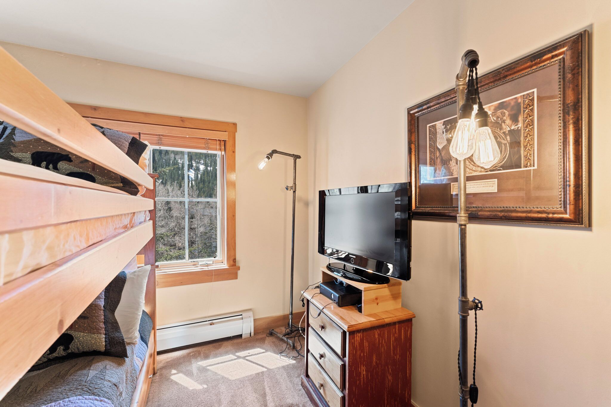 Una habitación con una cama litera, un televisor de pantalla plana, un cuadro enmarcado y una lámpara de pie.