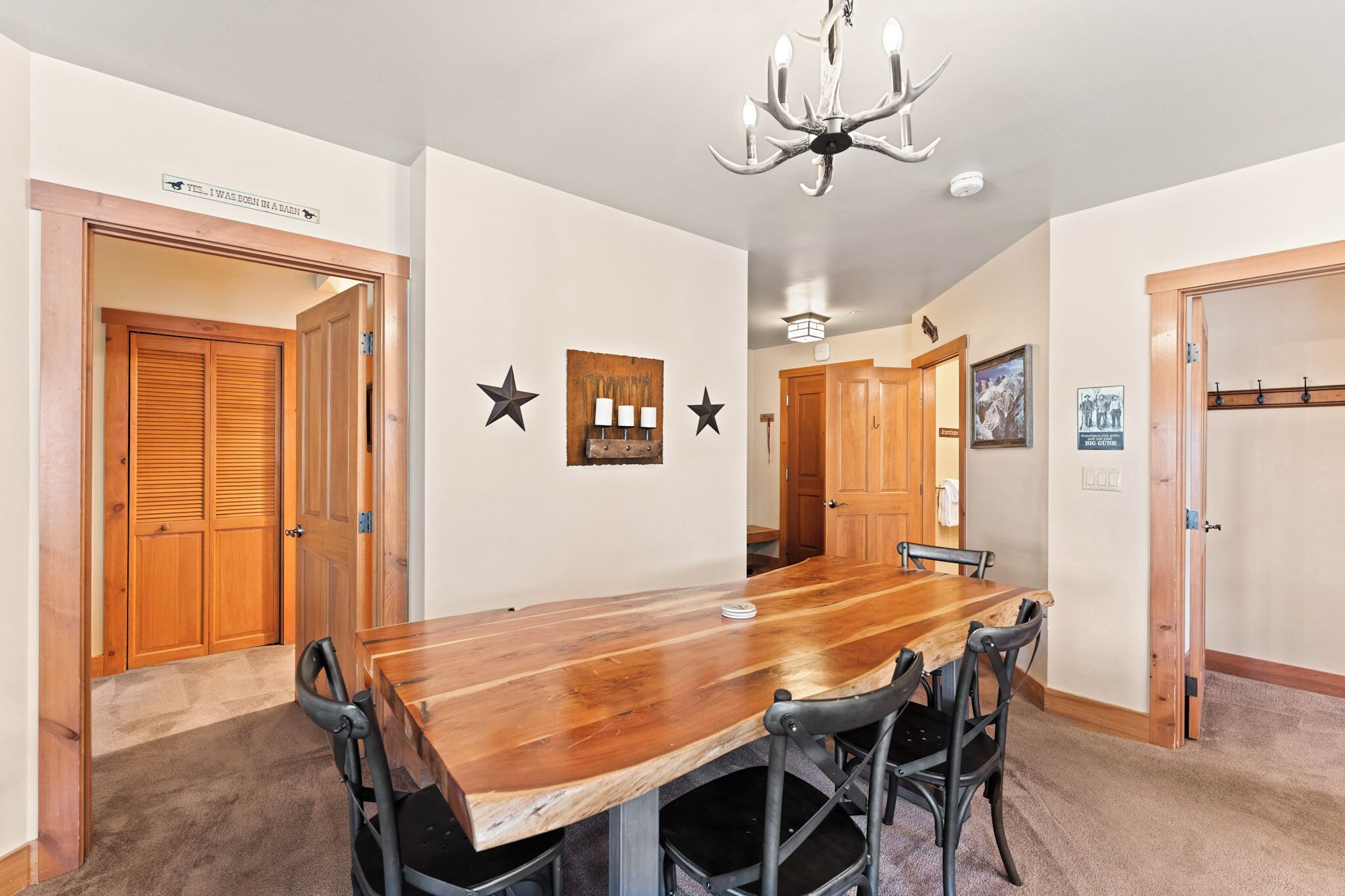 Een eetkamer met een houten tafel en stoelen, een kroonluchter en een bordje aan de muur.