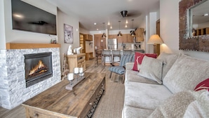 A modern living room with a fireplace, a sofa, and a dining area with chairs and a table. - Expedition Station #8583 (Keystone)