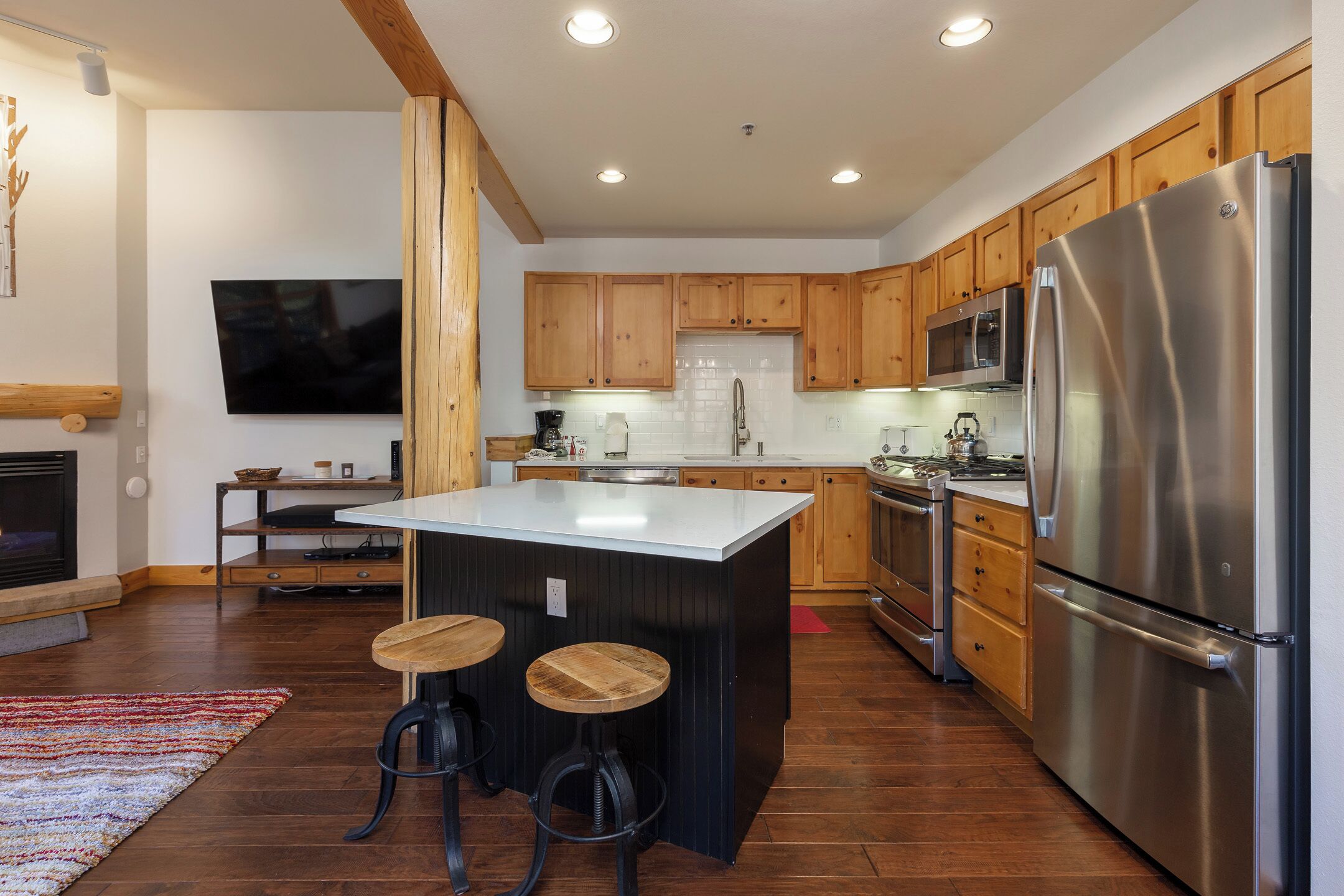 A modern kitchen with wooden cabinets, a stainless steel refrigerator, and a central island with stools.