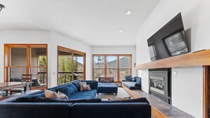 A modern living room with a large sectional sofa, a fireplace, and large windows offering a view of the outdoors. - Qs1645-2 (Keystone)