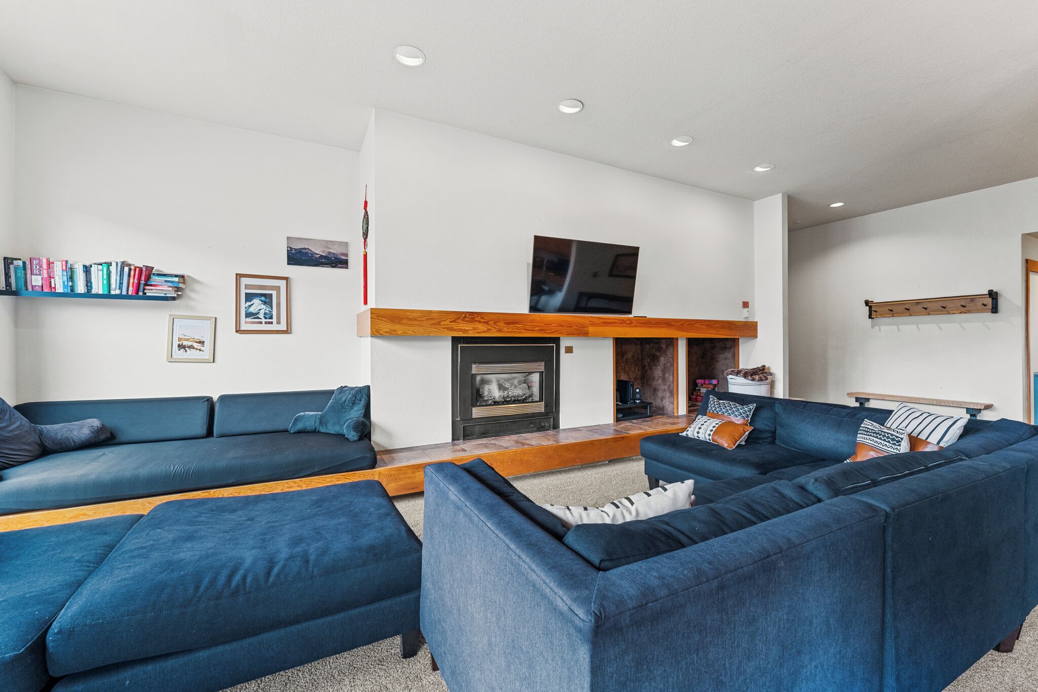 A modern living room with a fireplace, blue sofas, a bookshelf, and a mounted TV.