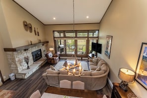 A spacious living room with a stone fireplace, a large window offering a view of the outdoors, a comfortable sofa, and a dining area.