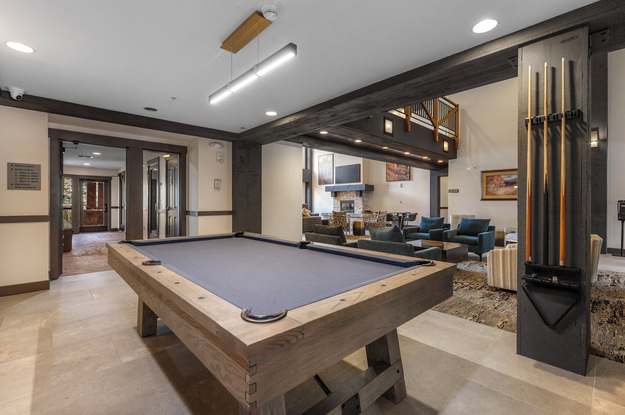 A pool table in a modern living area with a fireplace, comfortable seating, and a staircase leading to an upper level.
