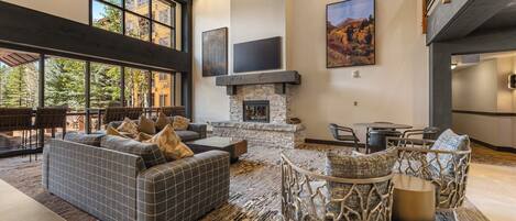 A spacious living area with a fireplace, large windows, and a high ceiling.
