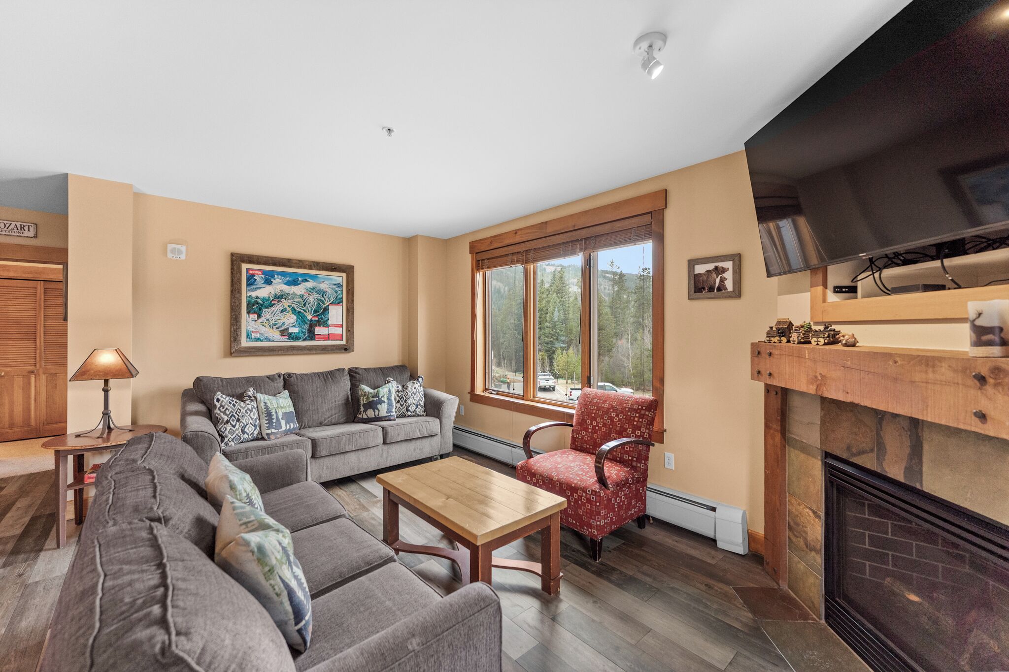 A living room with a fireplace, a sofa set, a coffee table, and a window with a view of trees.