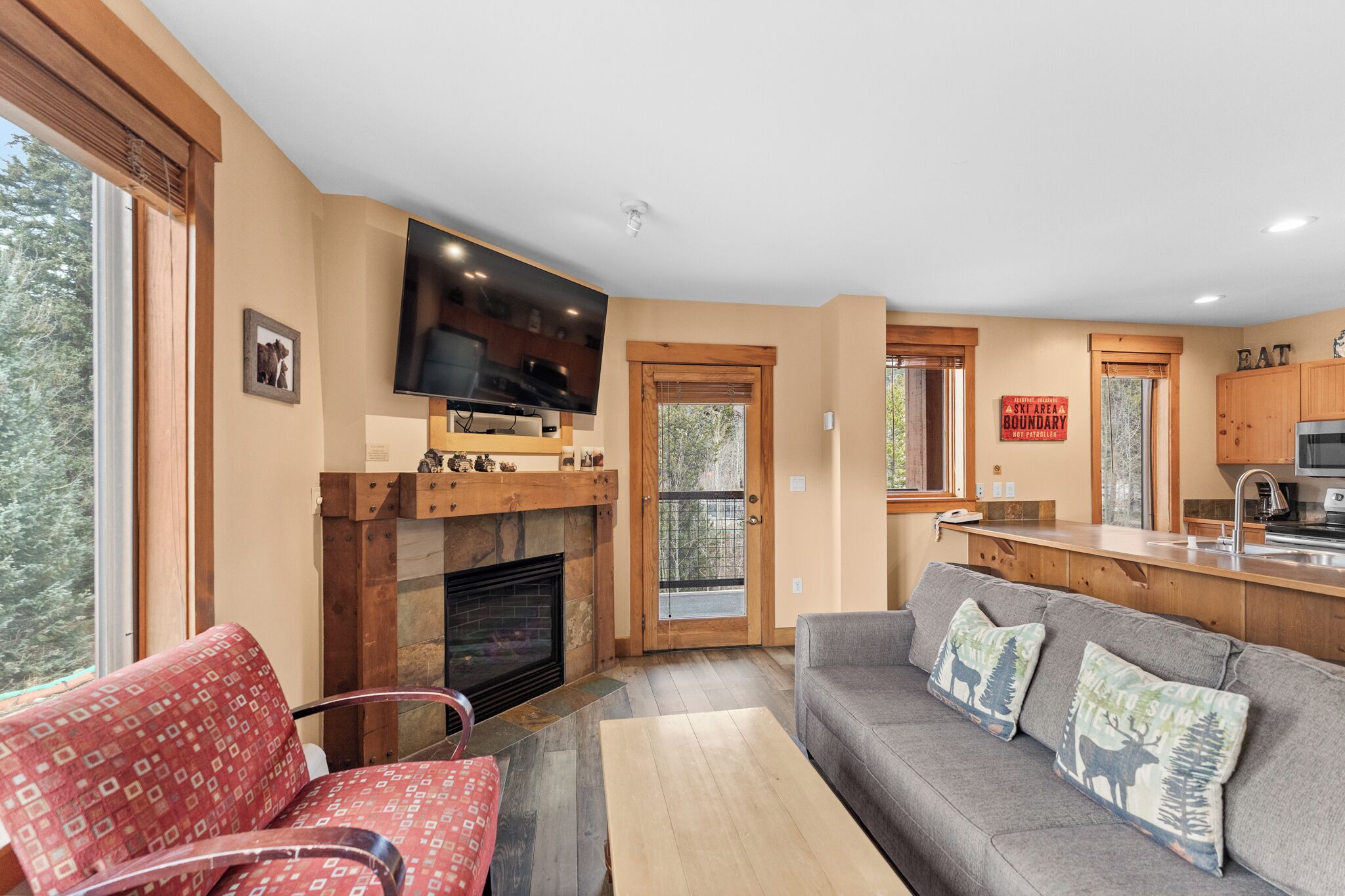 A cozy living room with a fireplace, a flat-screen TV, a sofa, and a dining area with wooden cabinets.