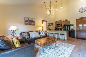 A living room with a sofa, coffee table, and a kitchen area with bar stools.