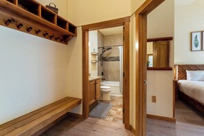 A bathroom with a shower, toilet, and sink. There is a wooden bench and a shelf with baskets.
