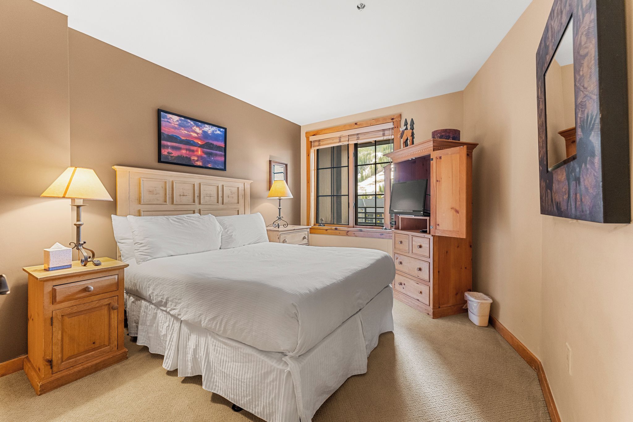 A bedroom with a large bed, wooden nightstands, a dresser, and a window with blinds.