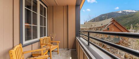 A balcony with wooden chairs, a window, and a view of a mountain.