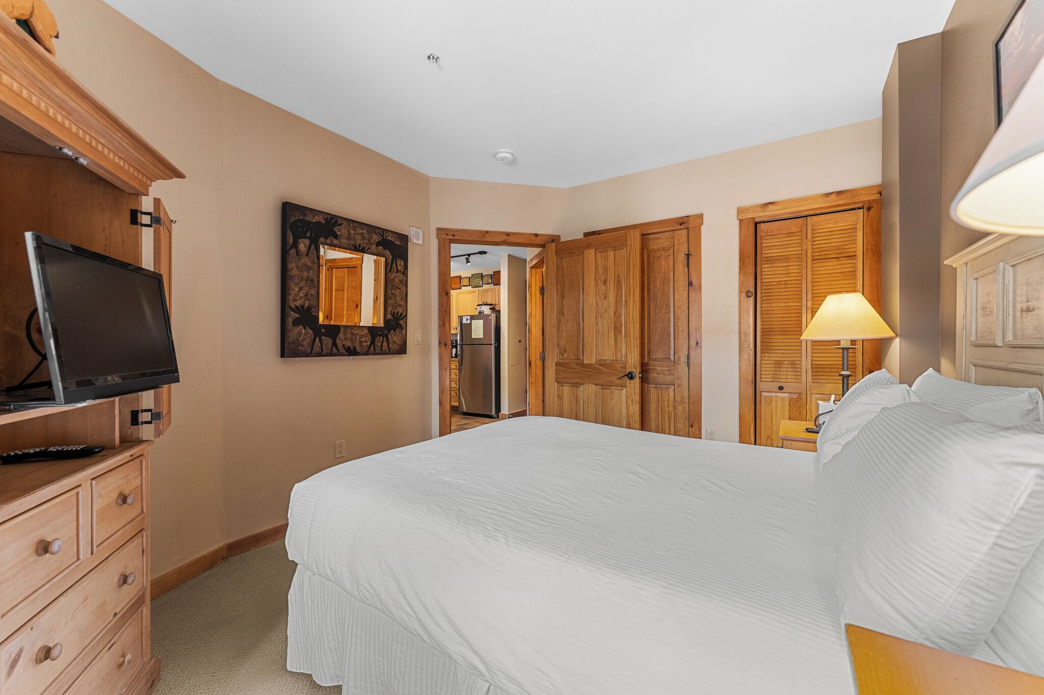 Un dormitorio con cama, armario de madera, televisor en una cómoda y un cuadro en la pared.