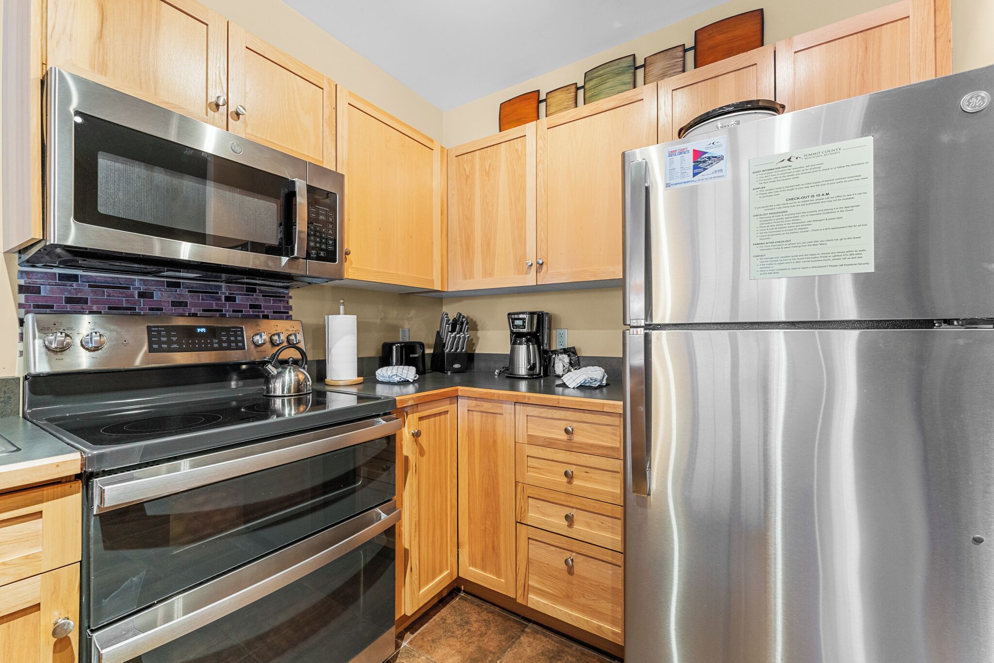 A modern kitchen with stainless steel appliances, wooden cabinets, and a built-in microwave.