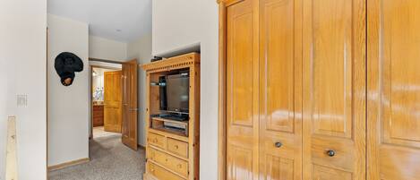 A hallway with wooden wardrobes, a built-in TV, and a coat rack.