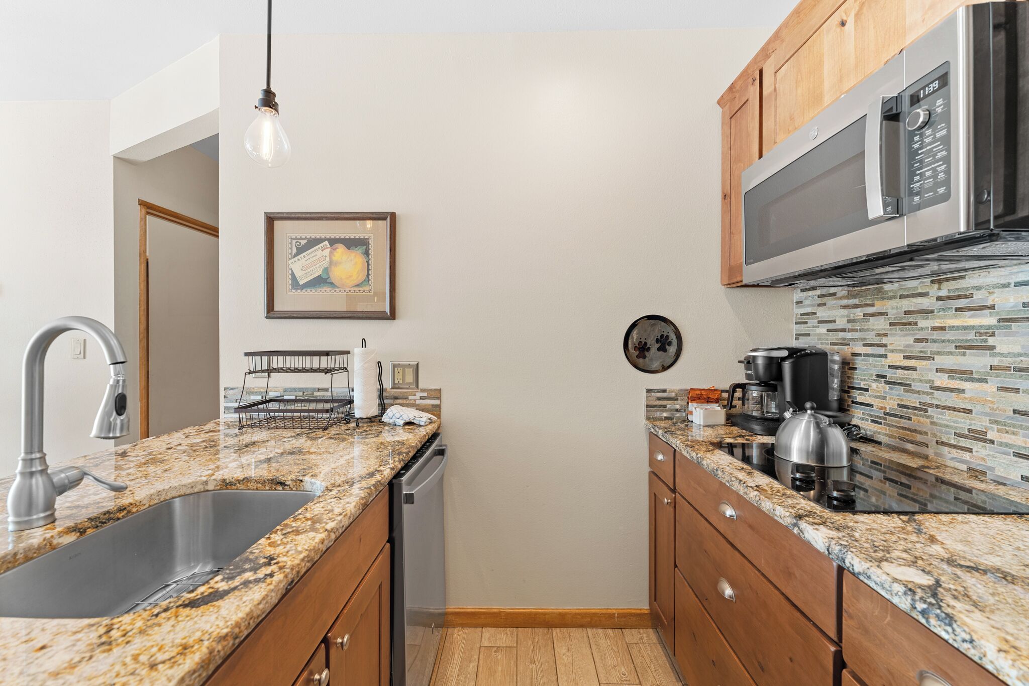 A kitchen with granite countertops, wooden cabinets, a stainless steel sink, a microwave, and a coffee maker.