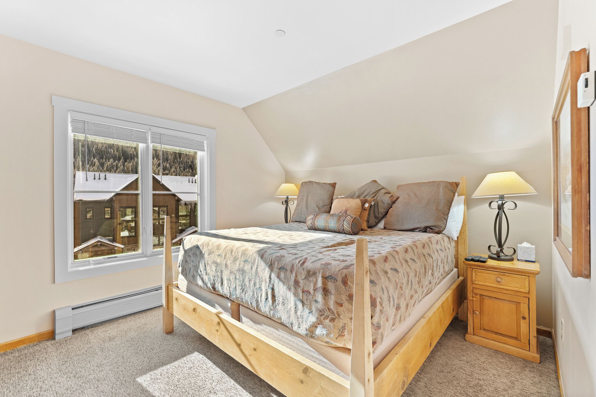 A bedroom with a wooden bed, two bedside lamps, a nightstand, a window with a view of buildings, and a ceiling light.