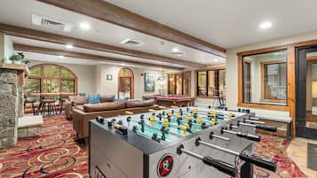 A room with a foosball table, a sofa, a dining table, and a fireplace.
