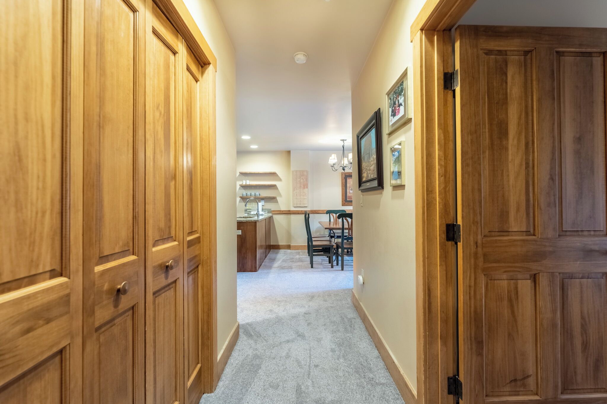 A hallway with wooden doors and a carpeted floor leading to a kitchen area with a dining table and chairs.