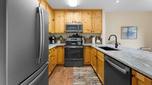 A modern kitchen with wooden cabinets, stainless steel appliances, and a granite countertop. - Snake River Village #29 (Keystone)