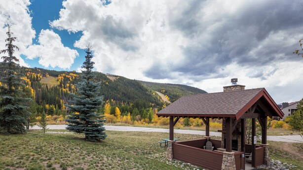 A wooden gazebo with a stone foundation, surrounded by a grassy area with a view of a forested mountain range. - Snake River Village #29 (Keystone)