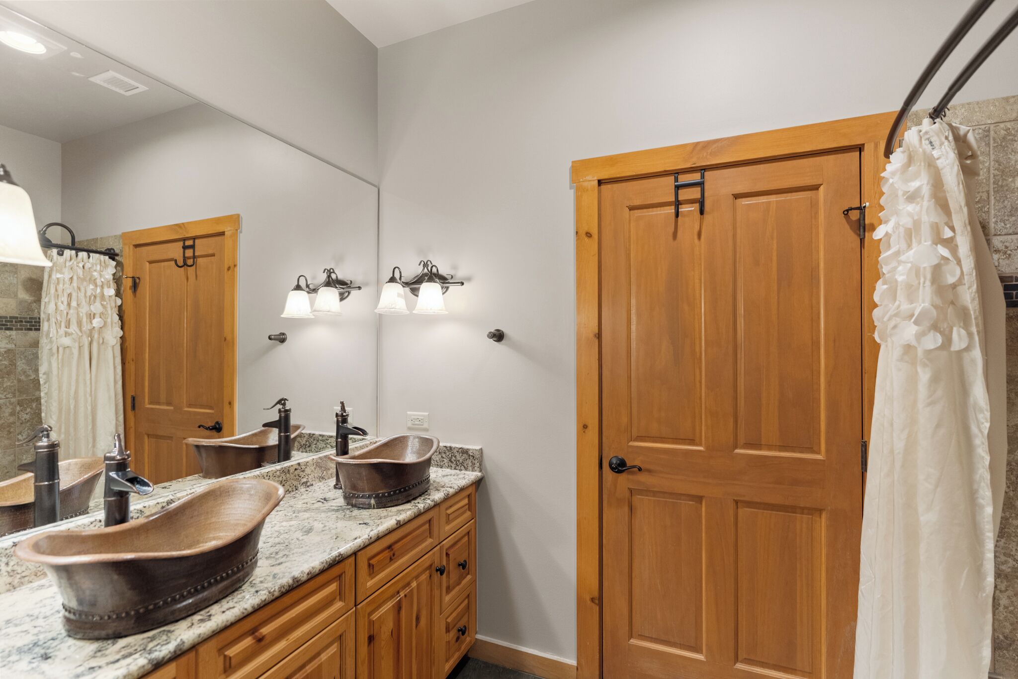 A bathroom with a wooden door, a large mirror, a vessel sink, and a shower curtain.