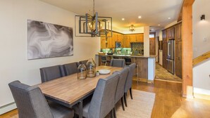 A dining area with a wooden table and grey upholstered chairs, a kitchen in the background, and a staircase leading to another level. - Ski Tip #8723 : 2 (Keystone)