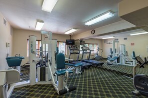 Academia com equipamentos de ginástica, um espelho e um relógio na parede.