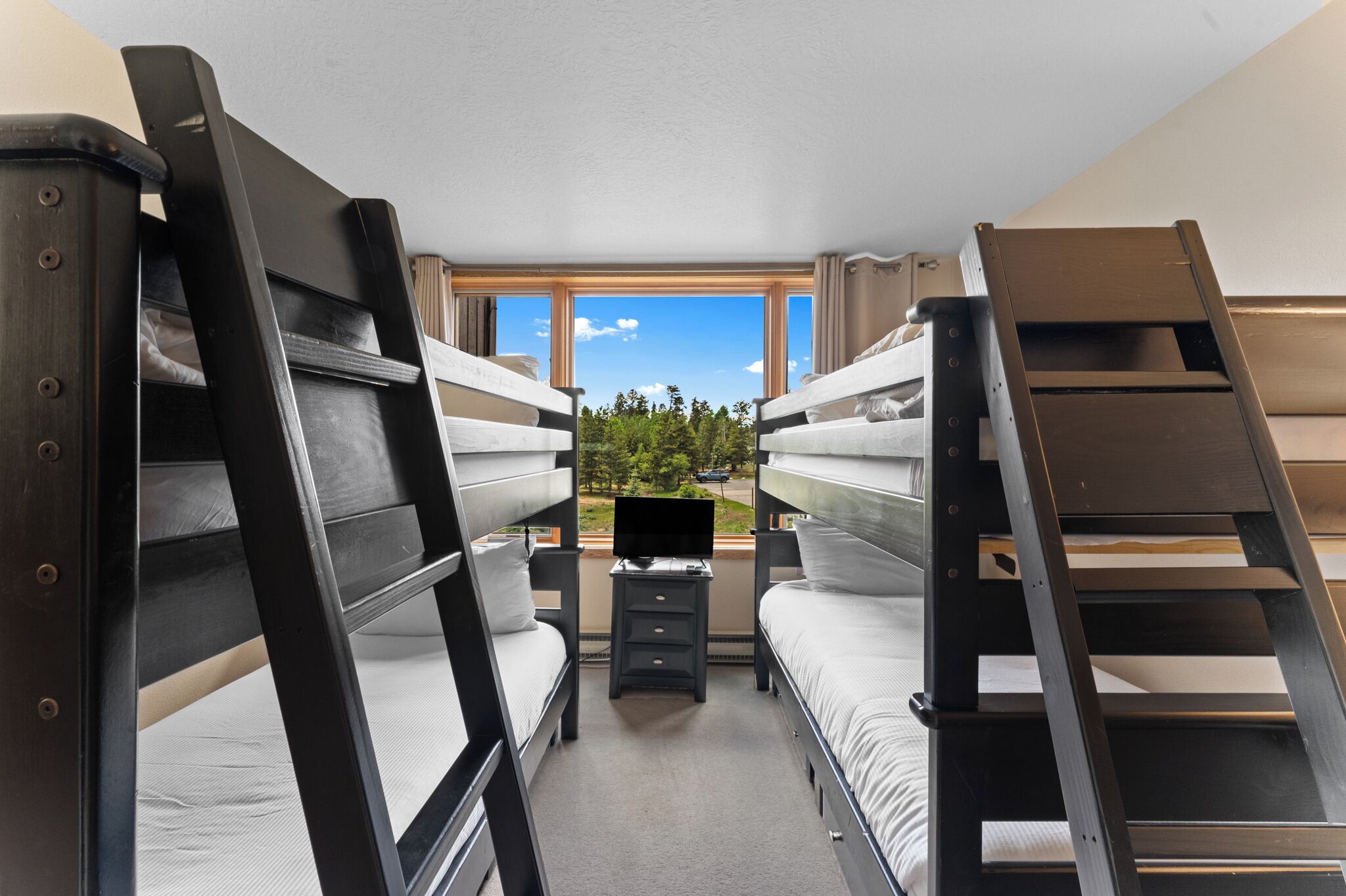 Une chambre avec deux lits superposés, un petit bureau et une fenêtre donnant sur des arbres et une route.