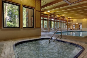 A hot tub area with a wooden ceiling, large windows, and a pool.