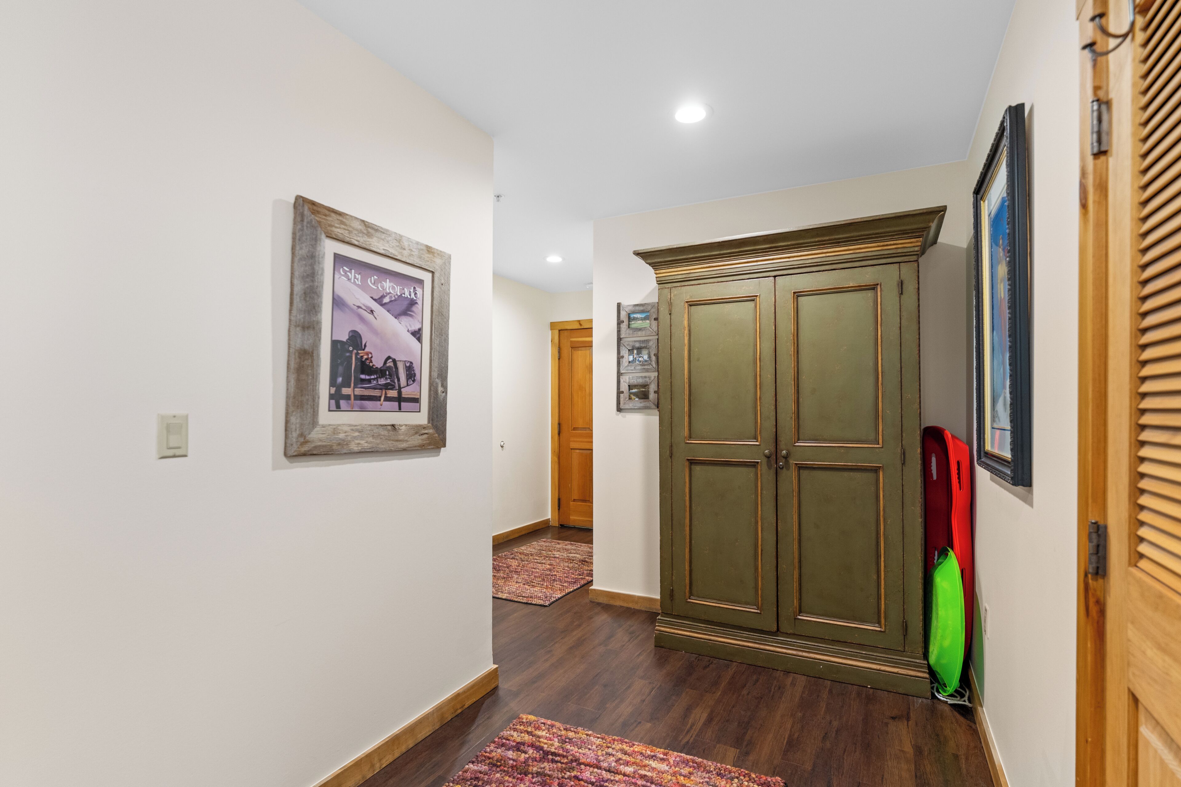 A hallway with wooden flooring, a green wardrobe, and a framed picture on the wall.