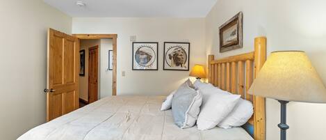 A bedroom with a bed, pillows, a wooden headboard, a bedside lamp, and two framed pictures on the wall.