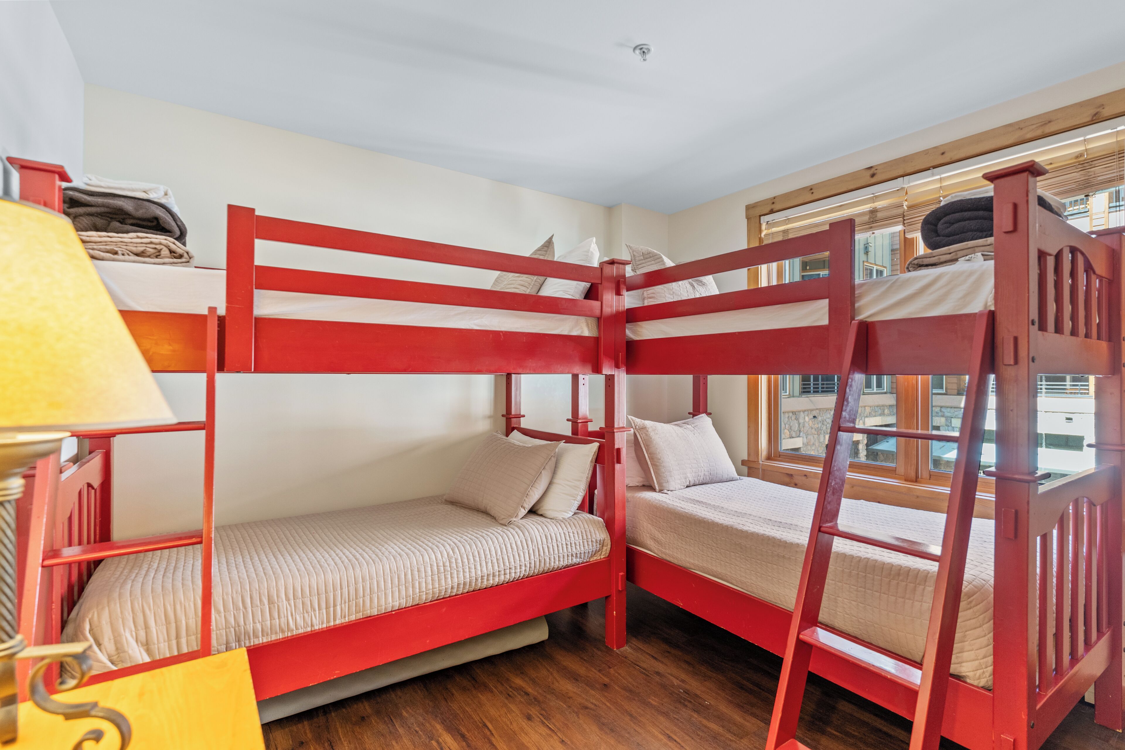 Une chambre avec deux lits superposés, un plancher en bois, une fenêtre avec vue et une lampe sur une table de chevet.
