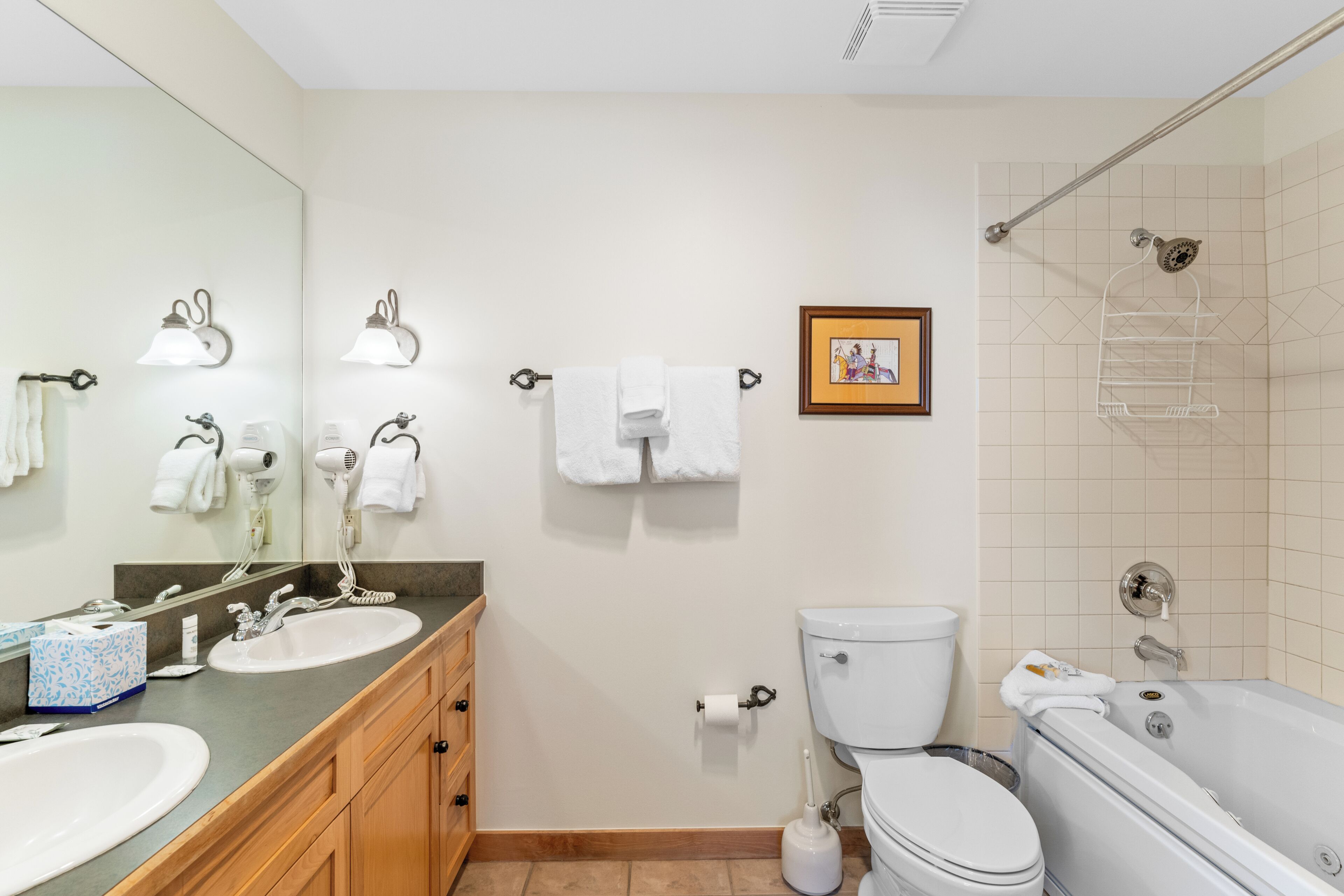 Une salle de bain avec un lavabo, des toilettes et une baignoire. Des serviettes sont accrochées à des crochets et un tableau encadré est accroché au mur.