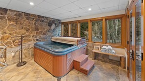 A hot tub with wooden steps, a stone wall, and a bench with towels. - Cdm2723 (Keystone)
