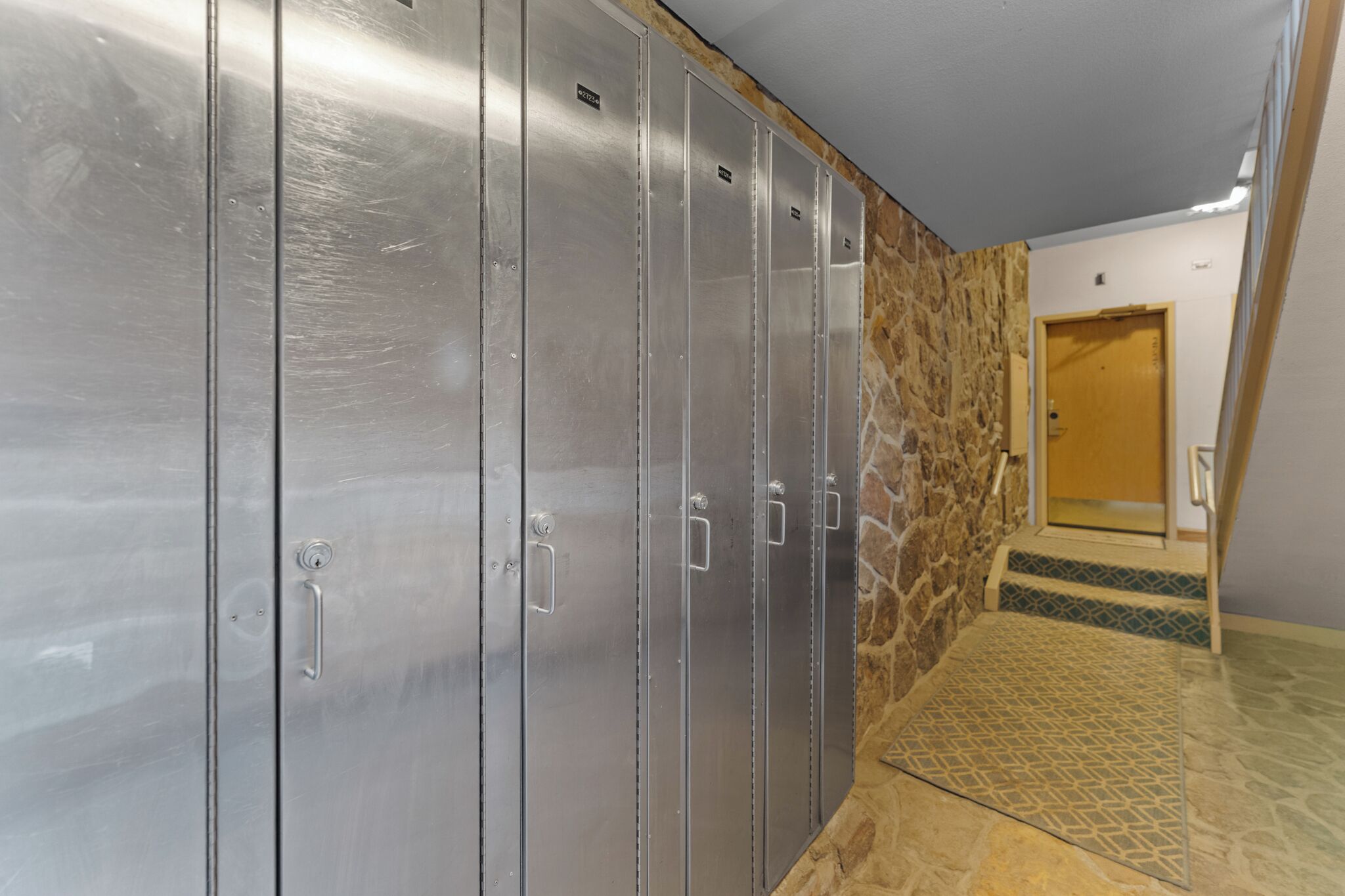 A row of metallic lockers with a stone wall and a wooden door in the background.