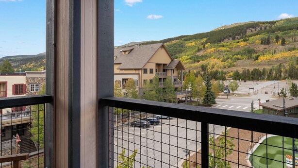 A view from a balcony overlooking a parking lot and a building with a sloped roof, surrounded by a hilly landscape with autumn foliage. - Dakota Lodge #8517 (Keystone)