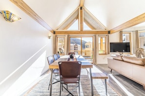 A spacious room with a high ceiling, a dining table with chairs, a sofa, and a TV.
