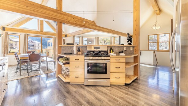 A spacious kitchen with wooden beams, a central island, and a large window overlooking a mountainous landscape.