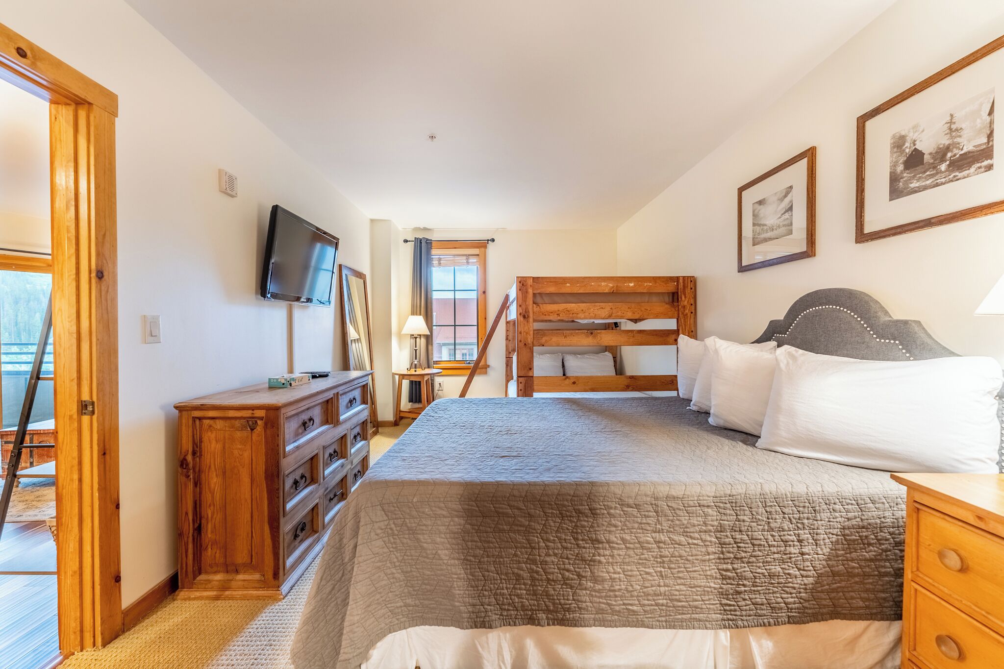 A bedroom with a bunk bed, wooden dresser, TV, and framed pictures on the wall.