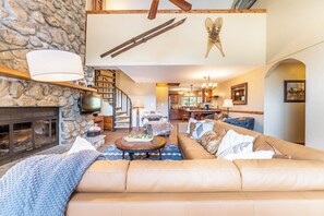 Una sala de estar acogedora con chimenea de piedra, un sofá grande y un comedor con candelabro.