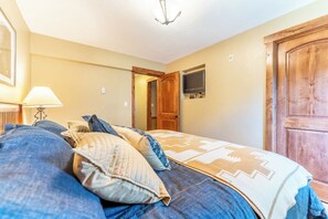 A bedroom with a bed, a TV mounted on the wall, and a wooden door.