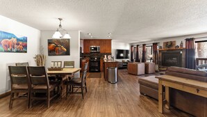 Un vaste espace de vie doté d’un plancher en bois, d’une table à manger avec des chaises, d’un canapé, d’une cheminée et d’un téléviseur.