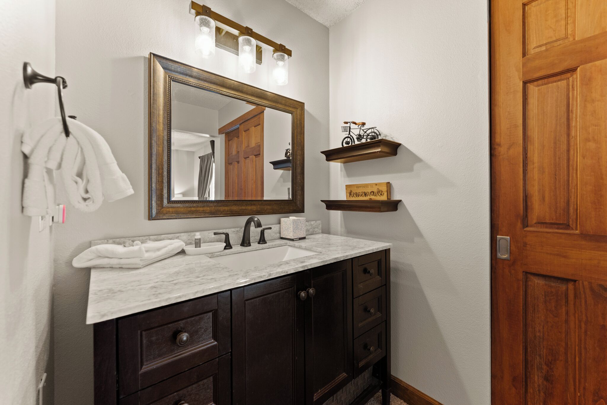 A bathroom with a marble sink, dark wooden cabinets, a large mirror, and a wooden door.