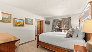 Une chambre avec un lit en bois, un téléviseur fixé au mur et trois tableaux représentant des paysages, encadrés.
