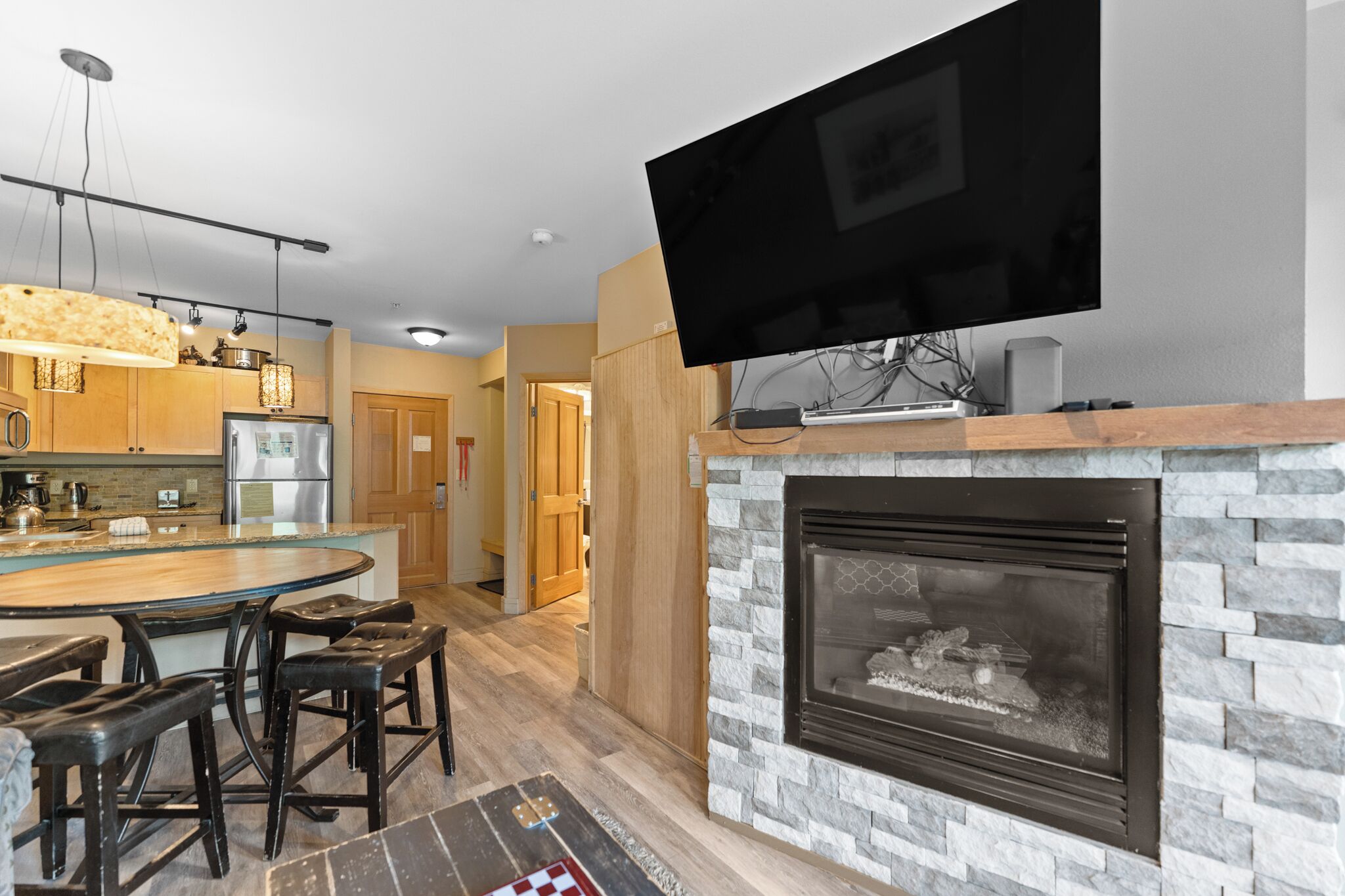 A modern kitchen with a stone fireplace, a flat-screen TV mounted above it, and a dining area with stools.