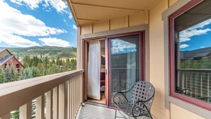 A balcony with a view of a mountainous landscape, a sliding glass door, and a metal chair. - Rh2299-1 (Keystone)