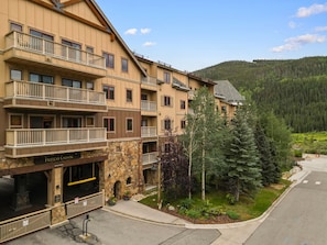 A multi-story hotel with balconies, a stone facade, and a view of a forested mountain.