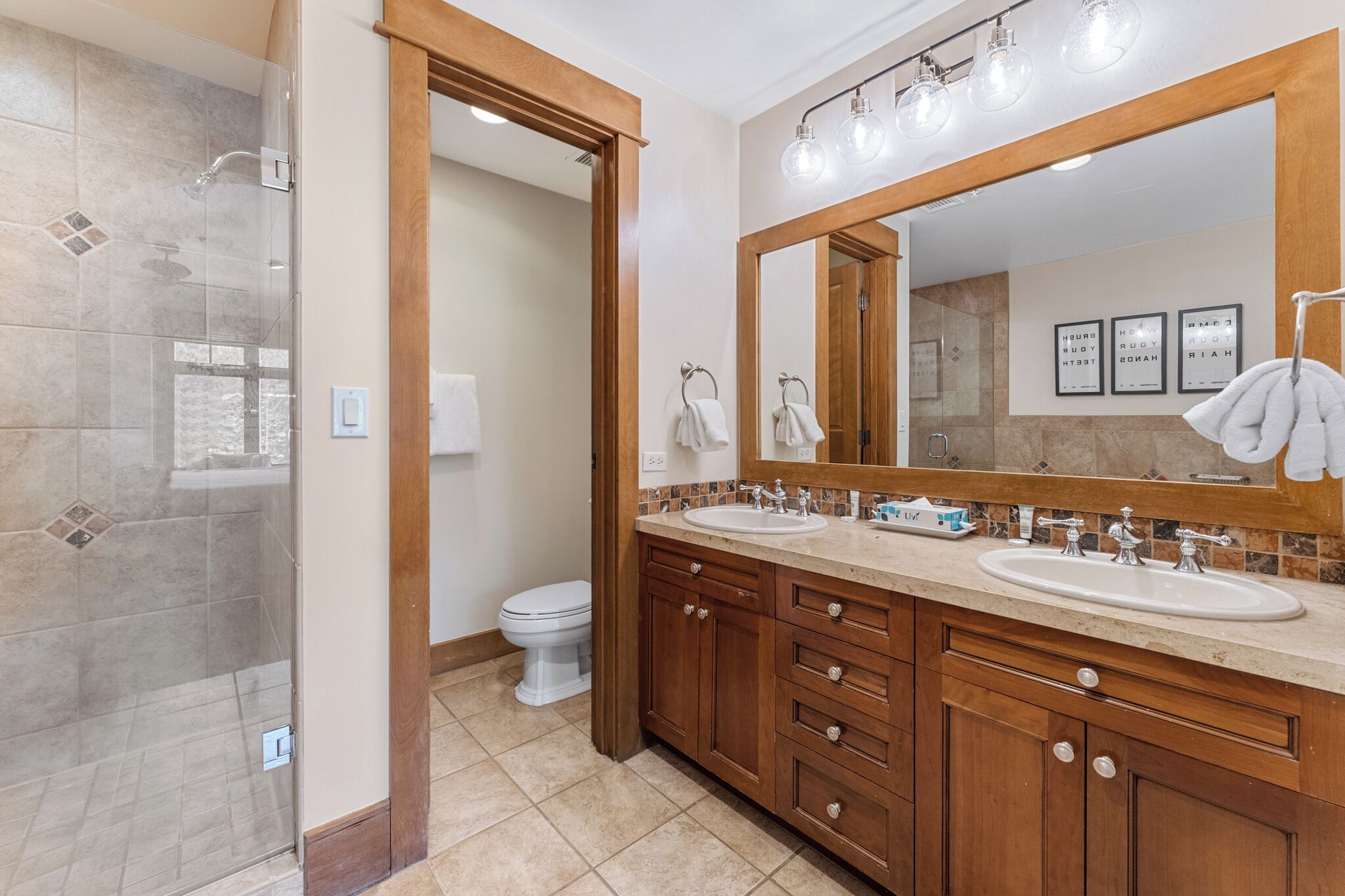 Une salle de bain avec une douche, deux lavabos, un grand miroir et des toilettes.