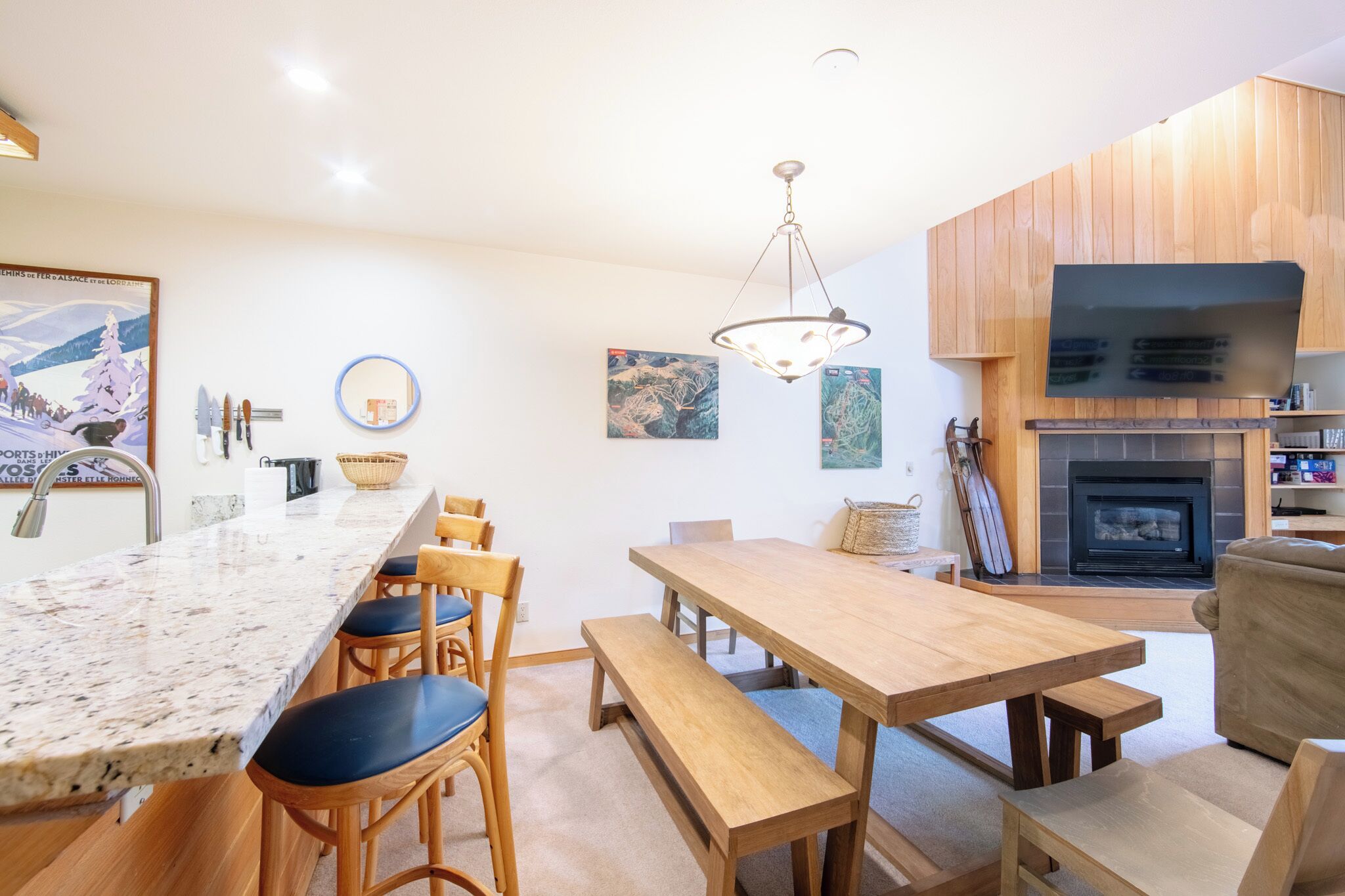 A modern kitchen with a marble countertop, wooden dining table, and bench seating.