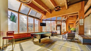 A pool table in a room with large windows, wooden beams, and a bench.
